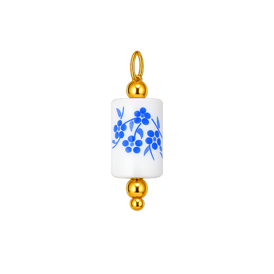 A cylindrical white ceramic pendant charm with a blue floral pattern, finished with polished gold-tone metal caps and a hanging loop at the top, shown on a plain white background.