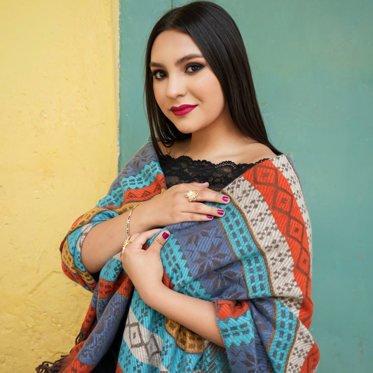 Colorful patterned shawl draped over her shoulders. The shawl features geometric and tribal-inspired patterns in blue, orange, beige, and gray.