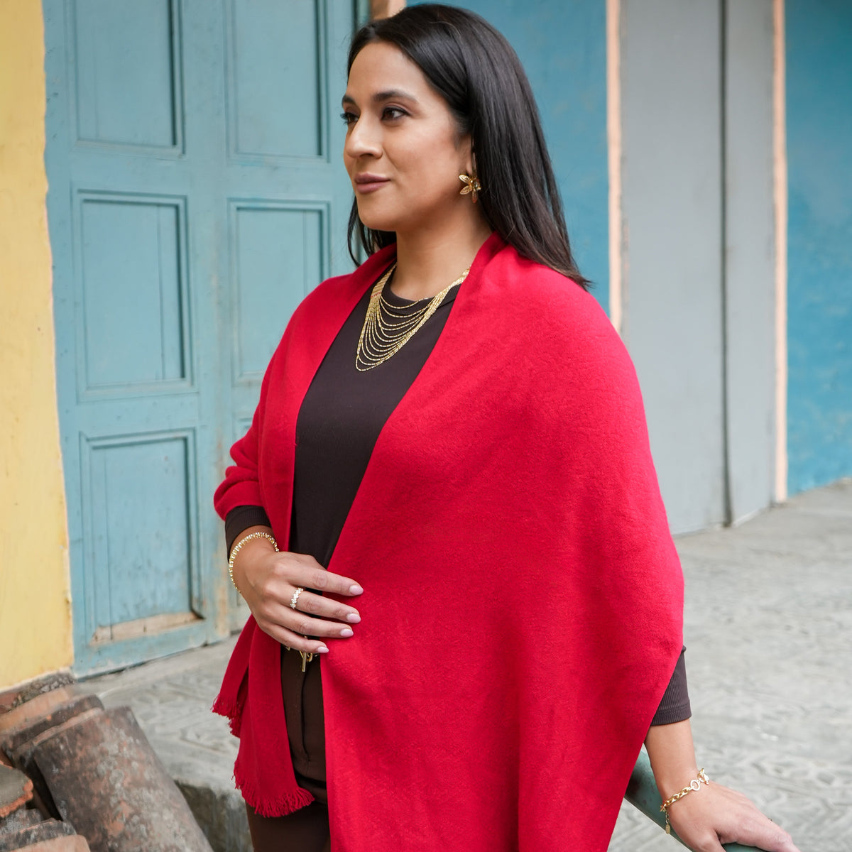 Red Ecuadorian alpaca scarf with fringed ends draped over the shoulders of a woman in brown, Alennya.